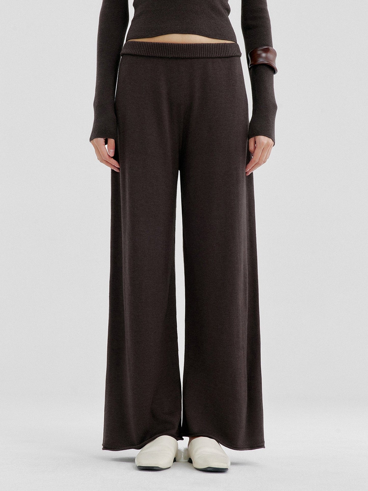 Woman wearing Arkin Studio relaxed drape knit pants in dark brown and matching top, hands down at her sides, wearing a pair of white shoes, standing facing the camera, on a white background