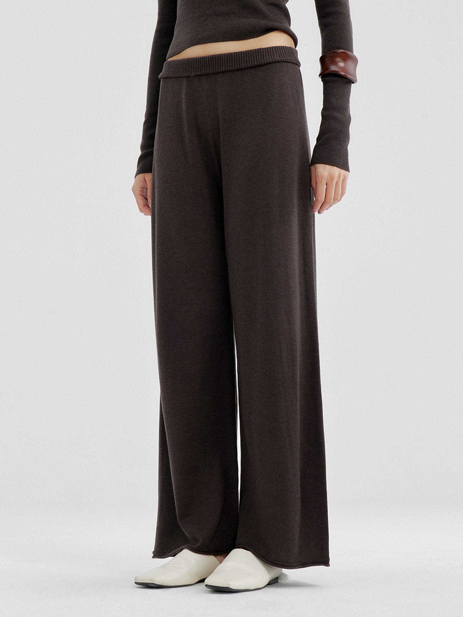 Woman wearing Arkin Studio relaxed drape knit pants in dark brown and matching top, hands down at her sides, wearing a pair of white shoes, standing sideways, on a white background