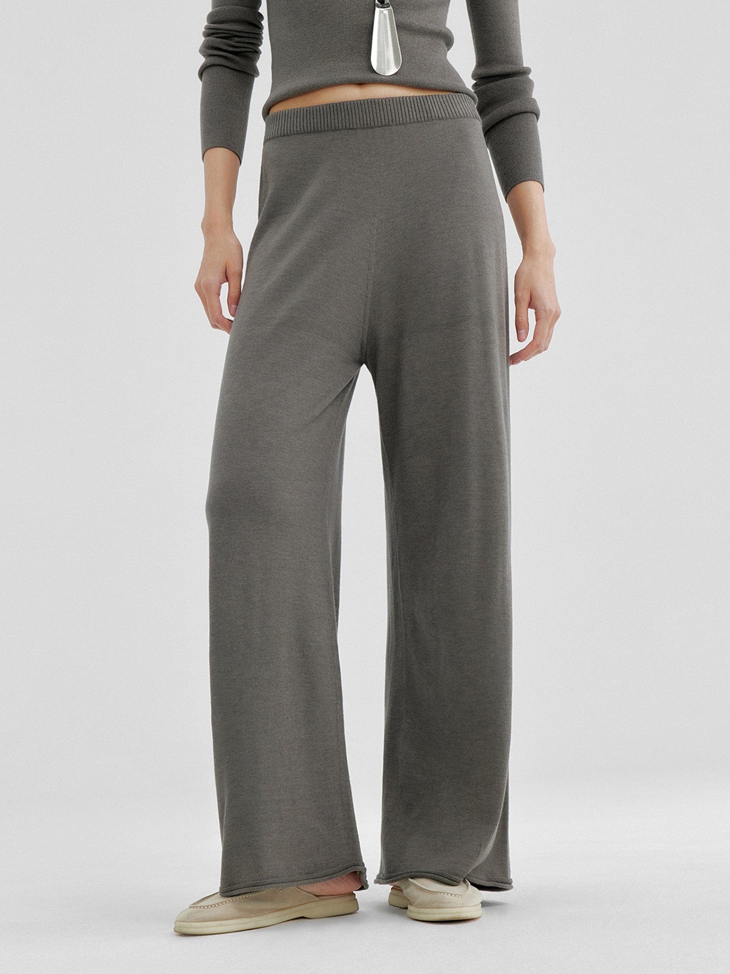 Woman wearing Arkin Studio relaxed drape knit pants in gray and matching top, hands down at her sides, wearing a pair of beige shoes, standing facing the camera, on a white background