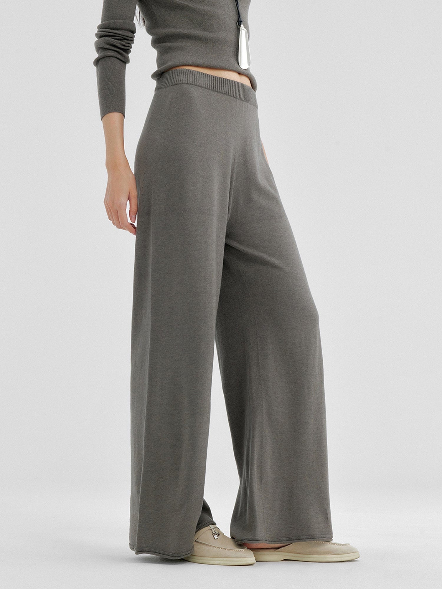 Woman wearing Arkin Studio relaxed drape knit pants in gray and matching top, hands down at her sides, wearing a pair of beige shoes, standing sideways, on a white background