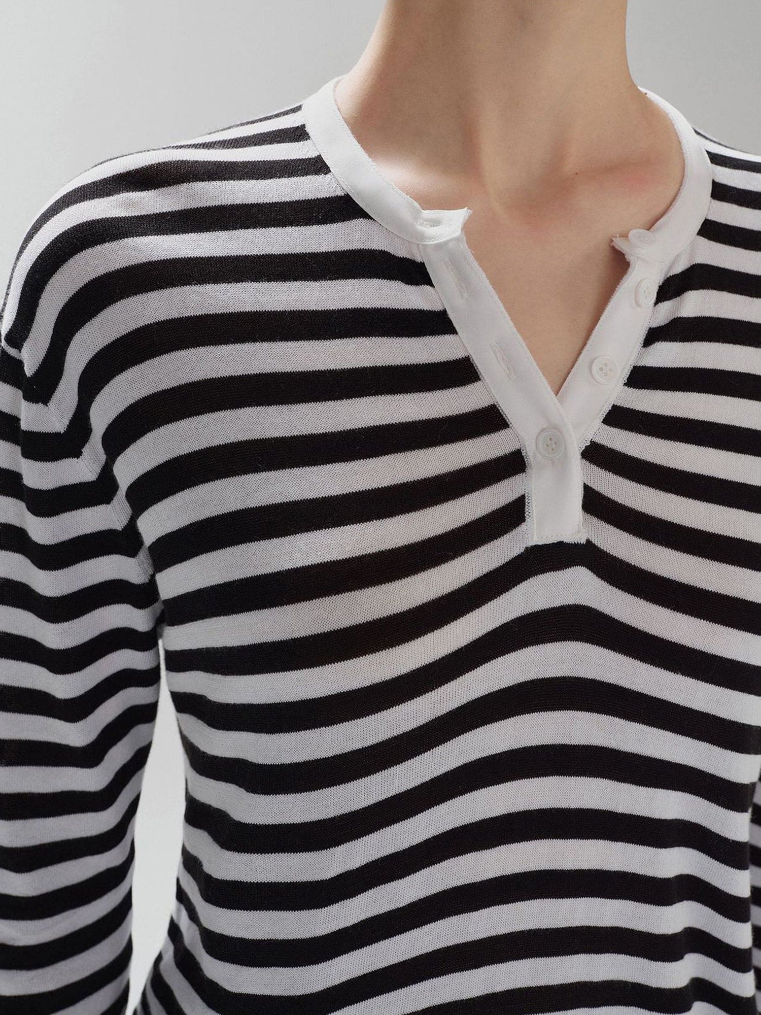 Close-up of a woman's chest wearing Arkin Studio black striped henley long sleeve tee, standing facing the camera, on a white background