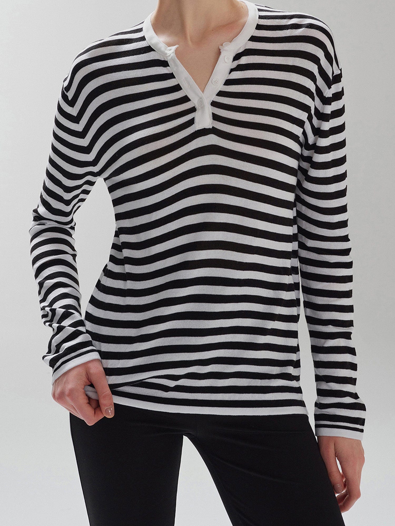 Woman wearing Striped Henley Long Sleeve Tee in Black and black leggings, standing facing the camera, on a white background