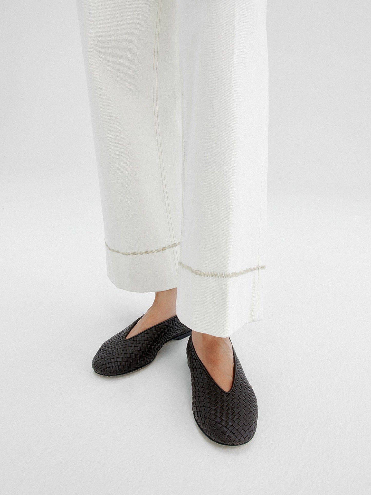 Close-up of a woman's legs from calf to feet wearing Arkin Studio white tailored cropped jeans with topstitching and black shoes, standing facing the camera, on a white background
