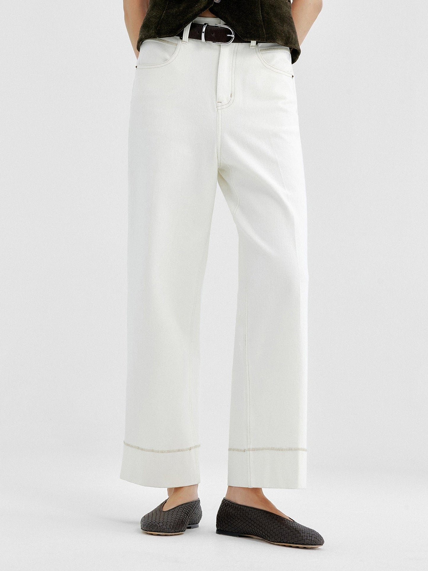 Woman wearing Arkin Studio tailored cropped jeans with topstitching in white and olive green top, wearing a pair of black shoes, standing facing the camera, on a white background