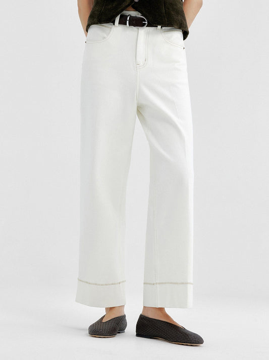 Woman wearing Arkin Studio tailored cropped jeans with topstitching in white and olive green top, wearing a pair of black shoes, standing facing the camera, on a white background