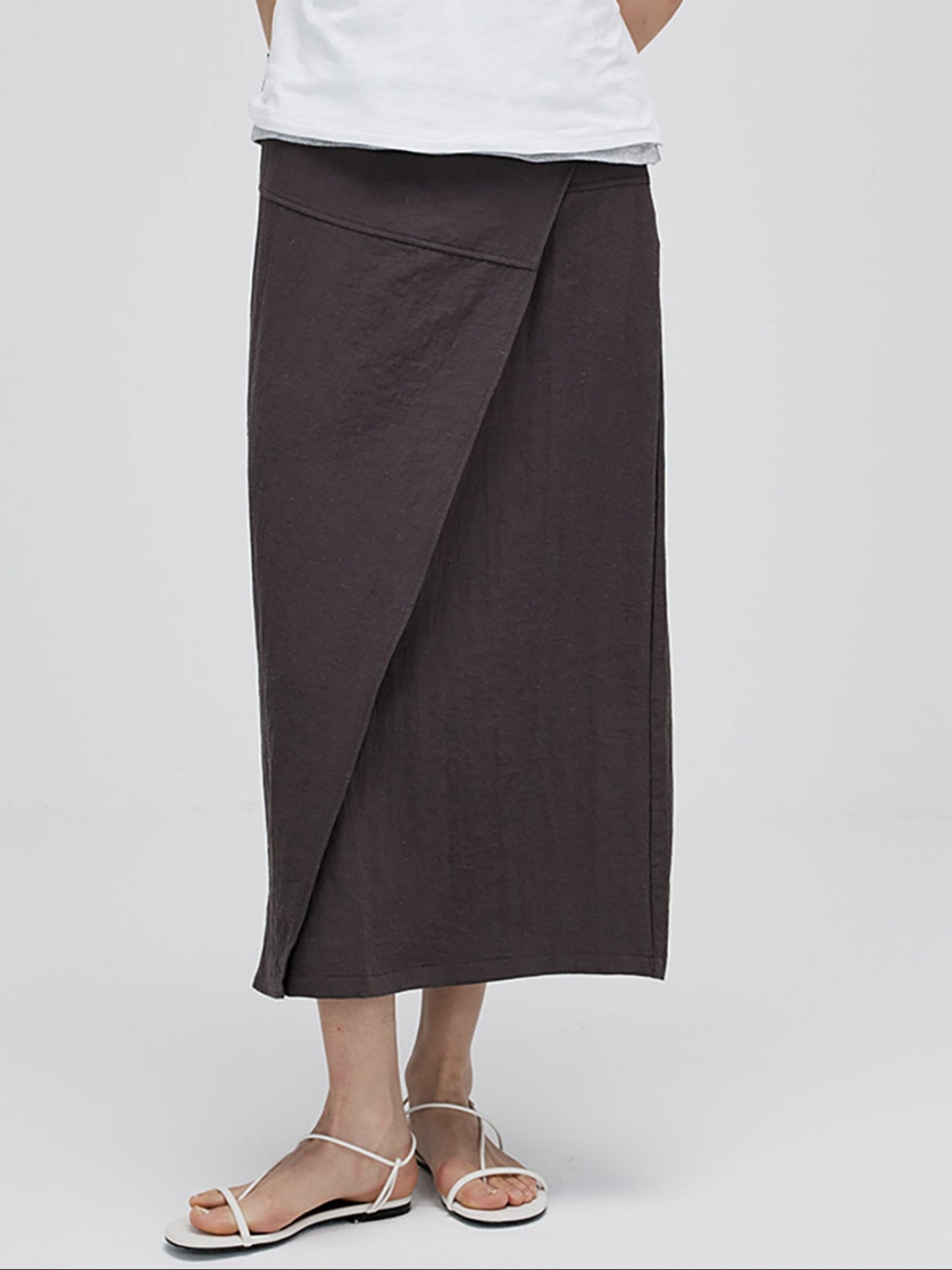 Woman wearing Arkin Studio textured h-line slit midi skirt with resin button in chocolate and a white top, standing facing camera, on white background