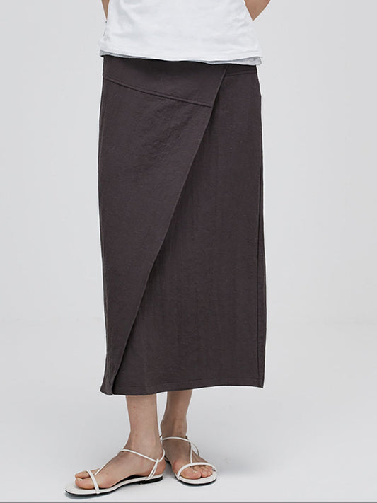Woman wearing Arkin Studio textured h-line slit midi skirt with resin button in chocolate and a white top, standing facing camera, on white background
