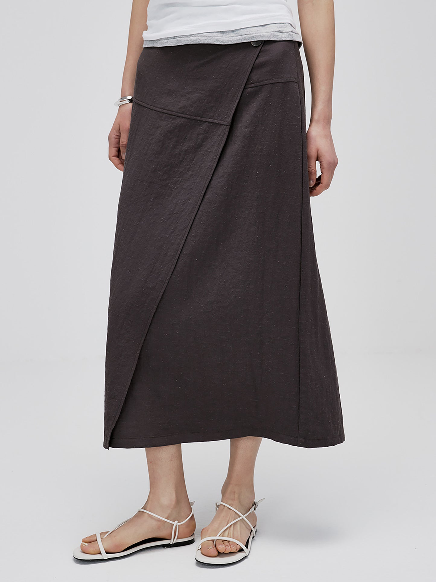 Woman wearing Arkin Studio textured h-line slit midi skirt with resin button in chocolate and a white top, standing facing camera, on white background