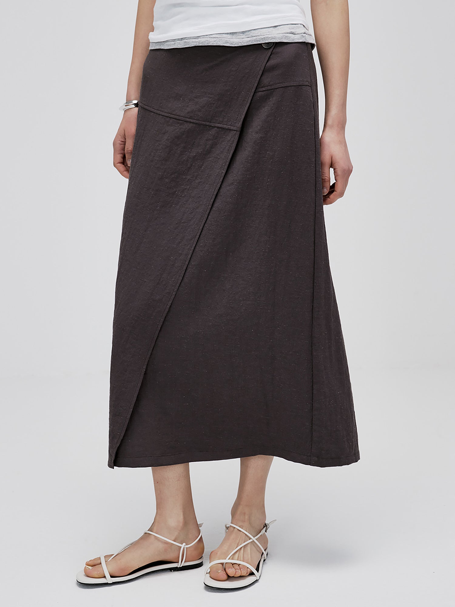 Woman wearing Arkin Studio textured h-line slit midi skirt with resin button in chocolate and a white top, standing facing camera, on white background
