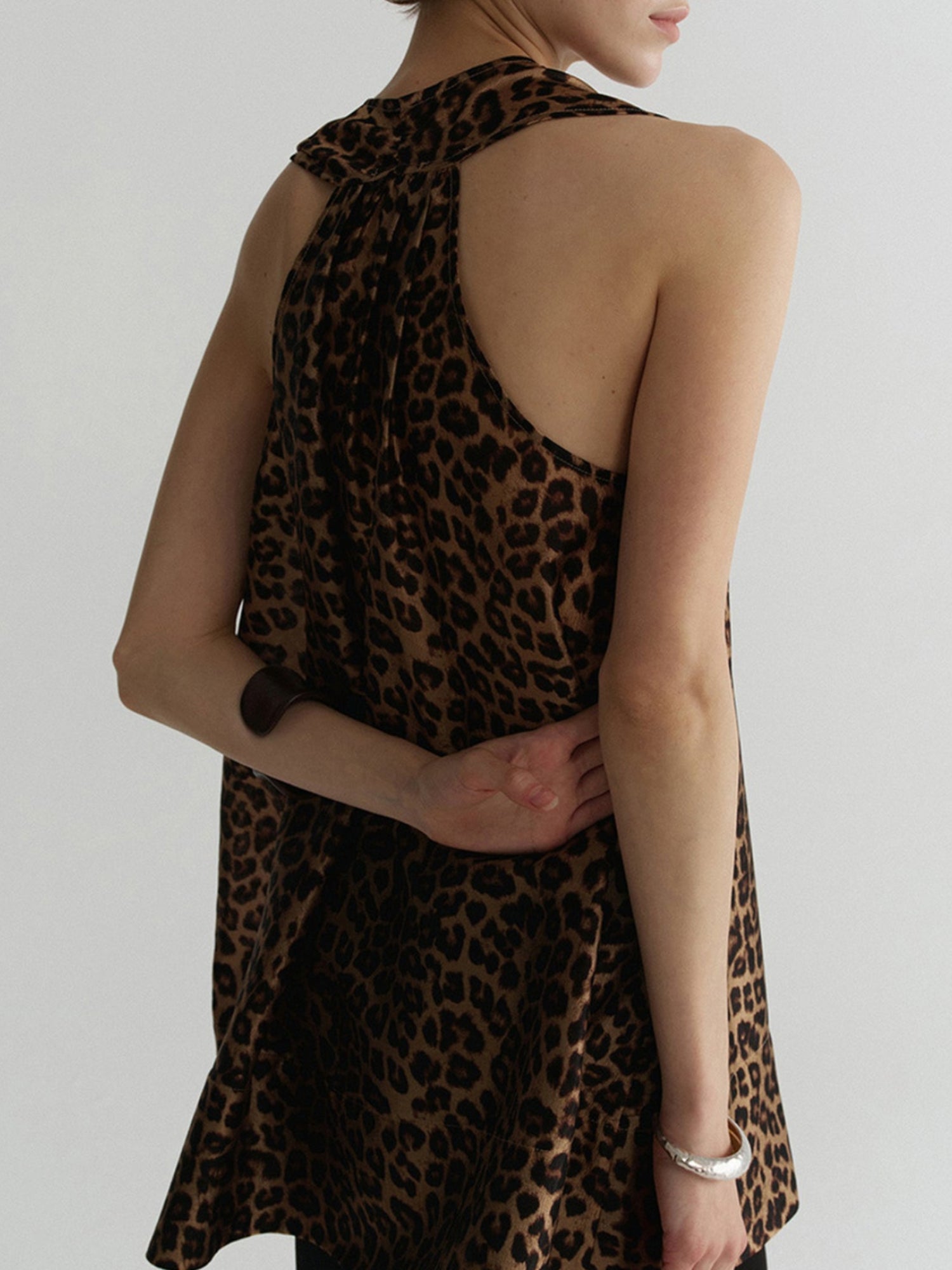 Woman wearing Arkin Studio wild leopard halter top with leopard pattern, standing back to the camera, on a white background