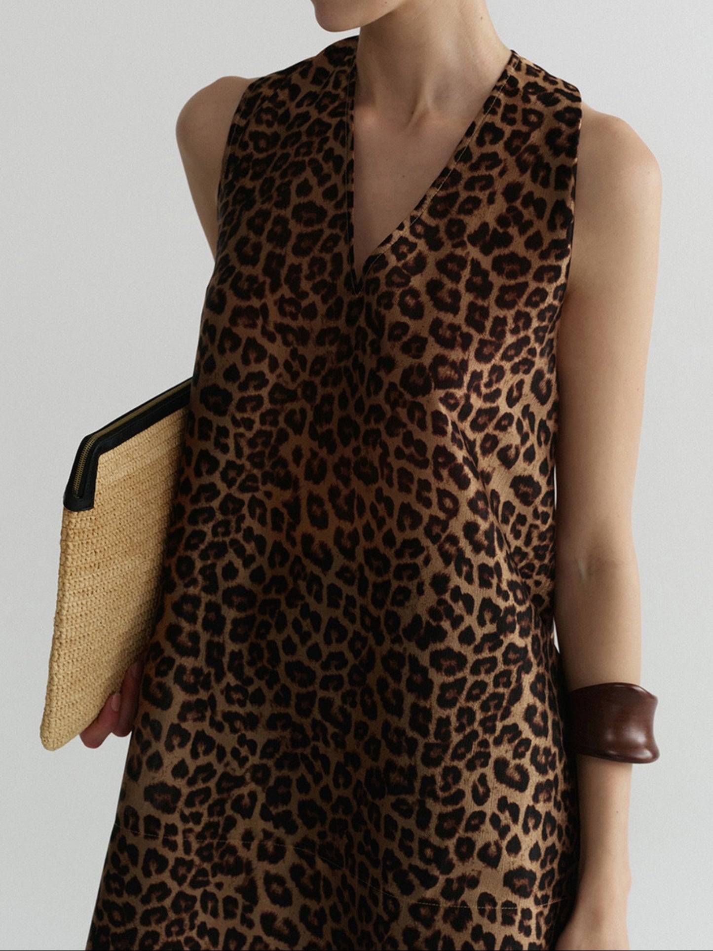 Woman wearing Arkin Studio wild leopard halter top with leopard pattern, holding a woven handbag, standing facing the camera, on a white background