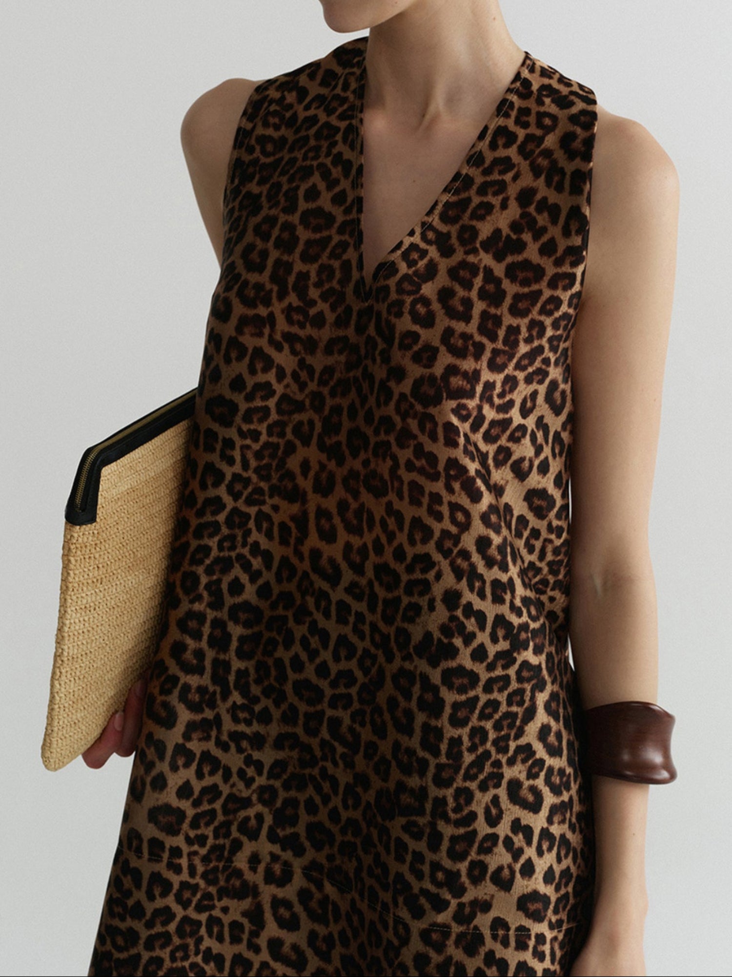 Woman wearing Arkin Studio wild leopard halter top with leopard pattern, holding a woven handbag, standing facing the camera, on a white background