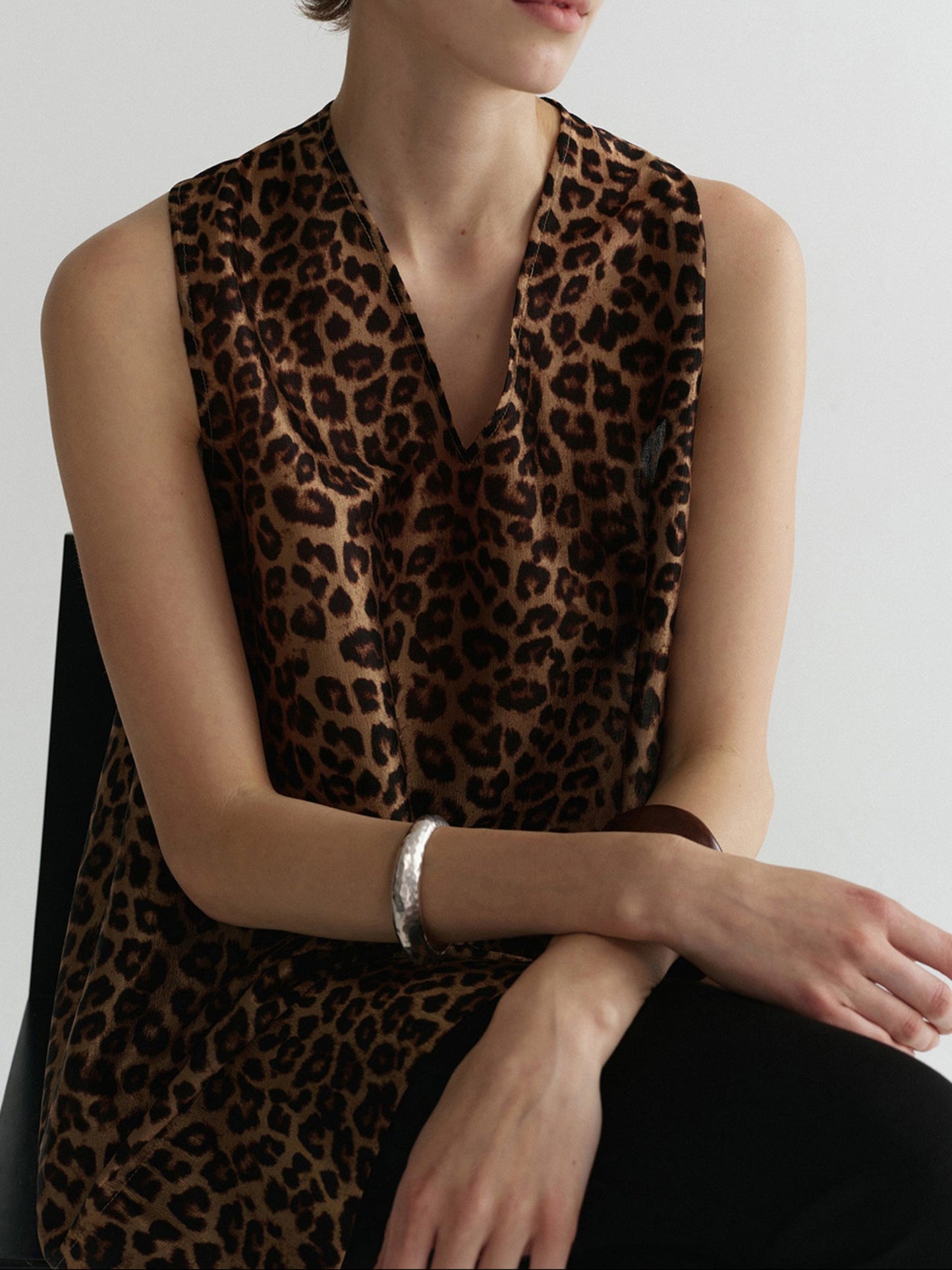 Woman wearing Arkin Studio wild leopard halter top with leopard pattern, sitting facing to the camera with arms crossed, on a white background