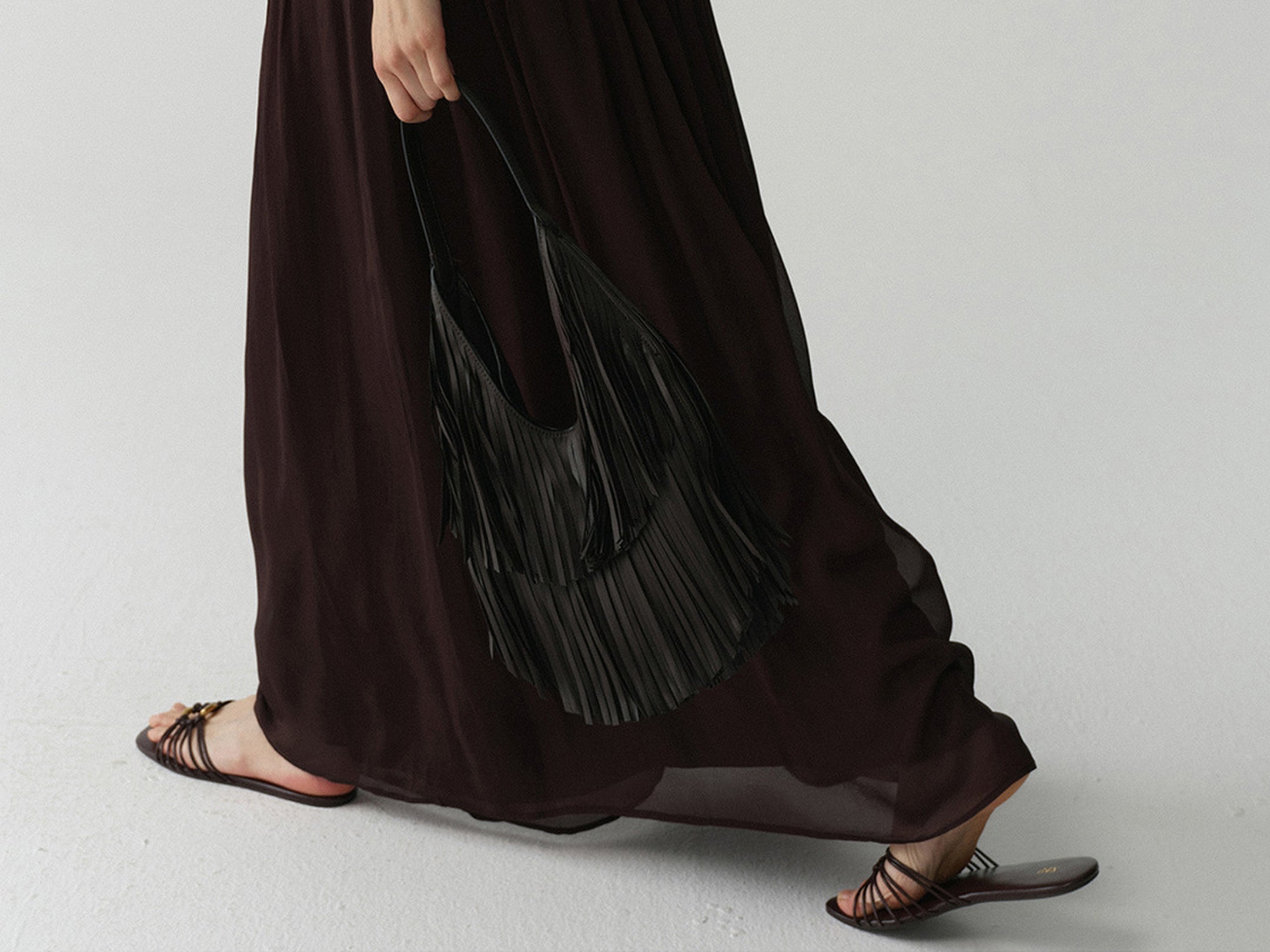 Close-up of a woman's lower body wearing Arkin Studio dark brown dress, walking, focusing on the wide swinging skirt hem and a black bag held in her hand